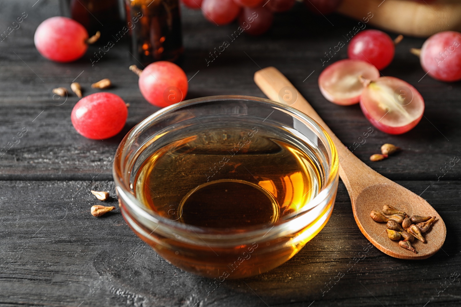 Photo of Glass bowl with natural grape seed oil on black wooden table. Organic cosmetic