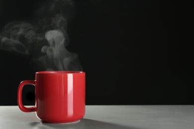 Mug with steam on table against black background. Space for text
