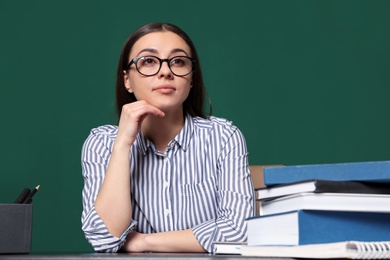 Portrait of young teacher at table against green background