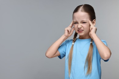 Photo of Little girl suffering from headache on grey background. Space for text
