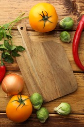 Empty cutting board and different vegetables on wooden table, flat lay. Space for text