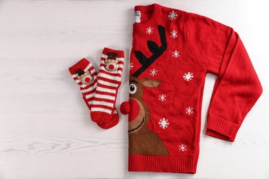 Photo of Christmas sweater and socks with pattern on wooden background, top view. space for text