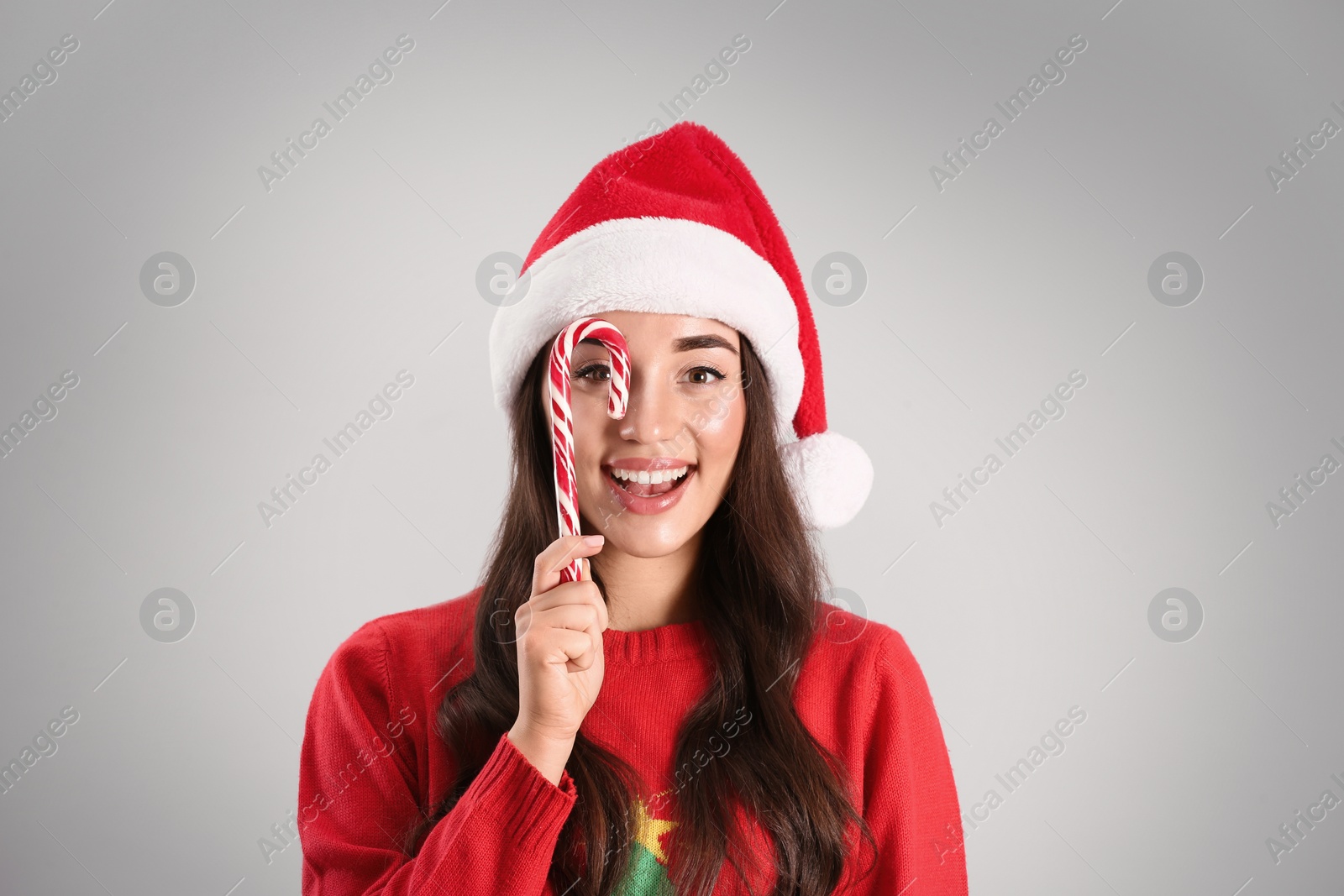 Photo of Beautiful woman in Santa Claus hat holding candy cane on light grey background