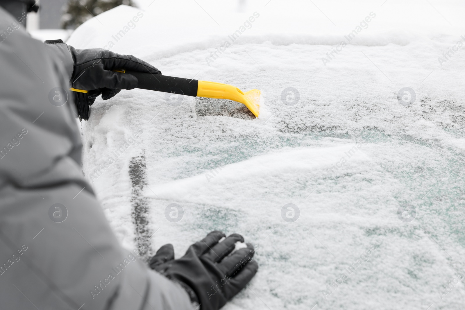 Photo of Man cleaning snow from car windshield outdoors, closeup