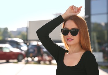 Beautiful woman in sunglasses on city street, space for text