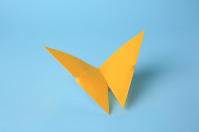 Photo of Origami art. Handmade yellow paper butterfly on light blue background