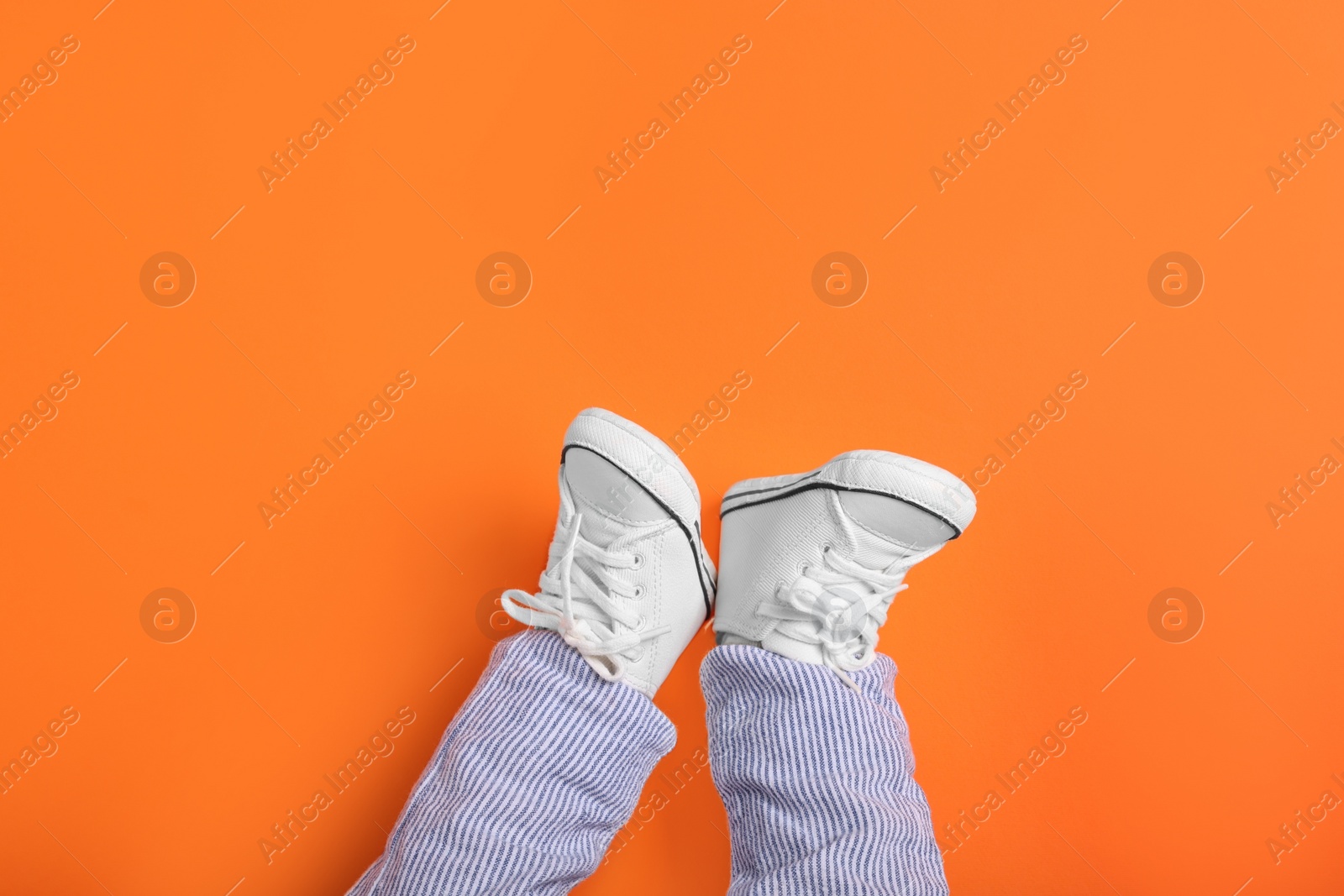 Photo of Little baby in stylish gumshoes on orange background, top view. Space for text