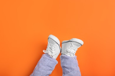 Photo of Little baby in stylish gumshoes on orange background, top view. Space for text