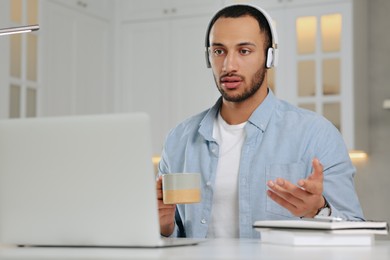 Photo of Young man with headphones having online video chat at desk in kitchen. Home office