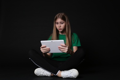 Photo of Shocked teenage girl with tablet on black background. Danger of internet