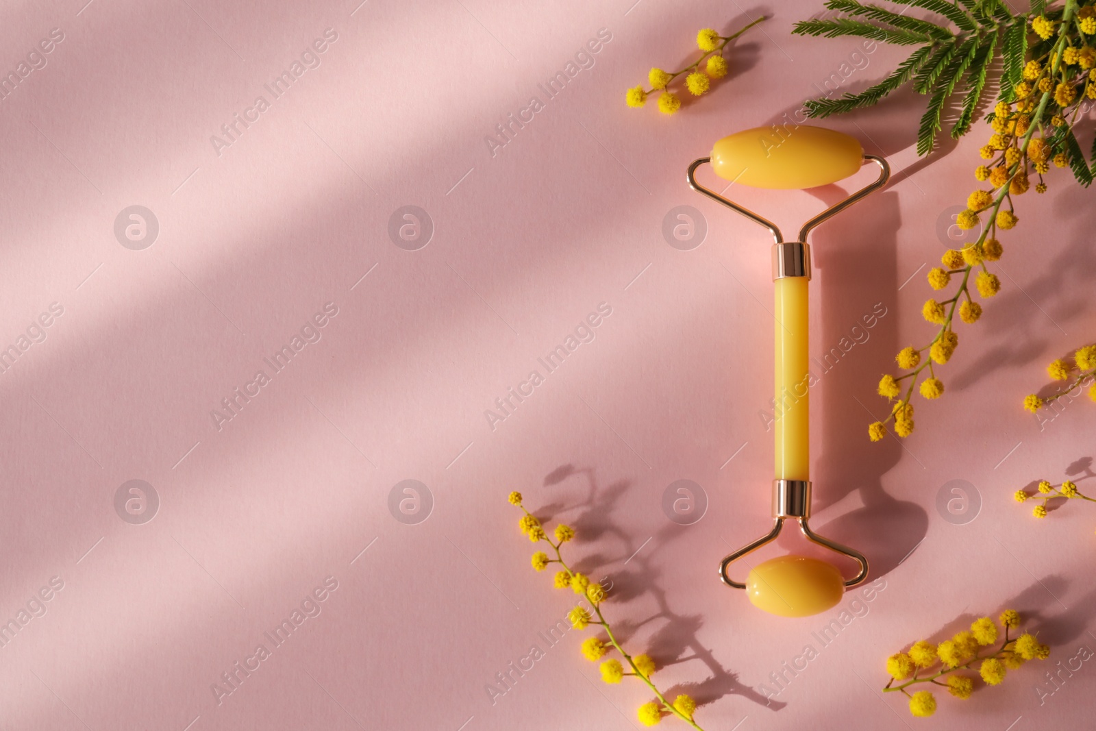Photo of Natural face roller and flowers on pink background, flat lay. Space for text