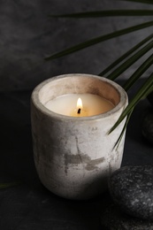 Photo of Palm leaf near burning candle and spa stones on dark table