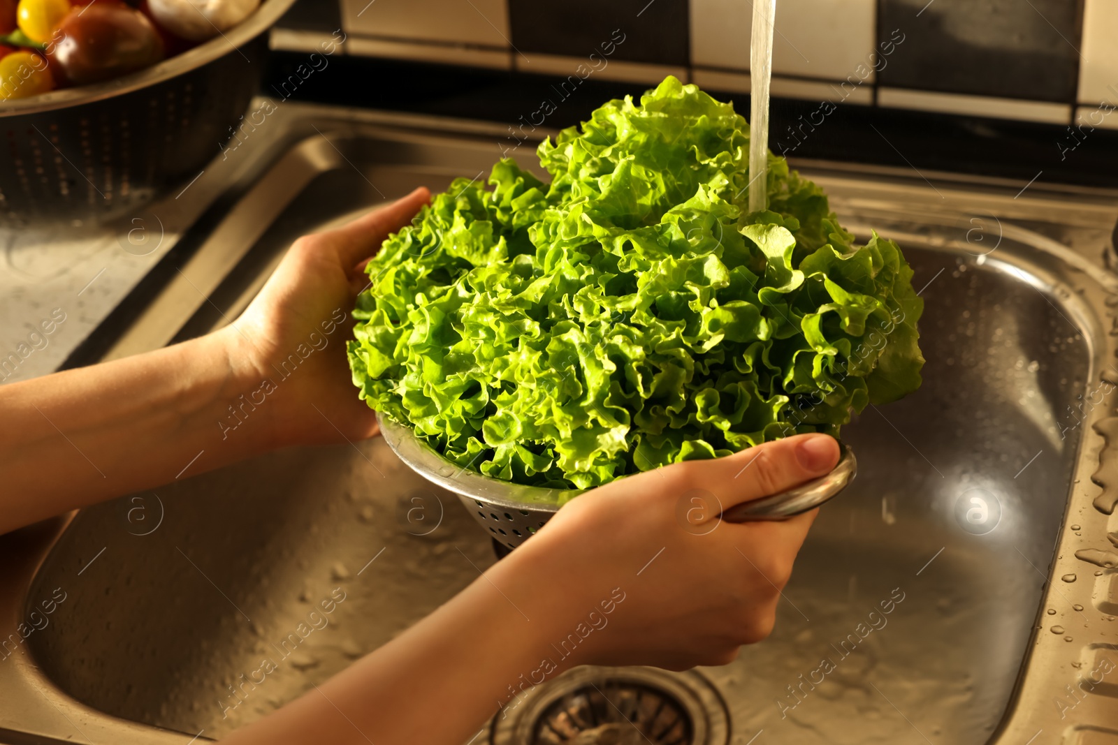 Photo of Woman washing fresh lettuce leaves in metal colander, closeup