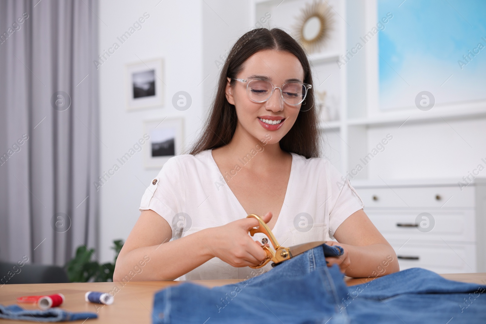 Photo of Happy woman cutting hem of jeans at table indoors