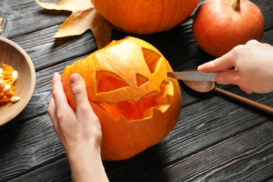 Photo of Woman carving Halloween pumpkin head jack lantern on wooden table, closeup