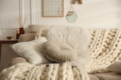 Photo of Beige sofa with knitted blanket and cushions in room. Interior design