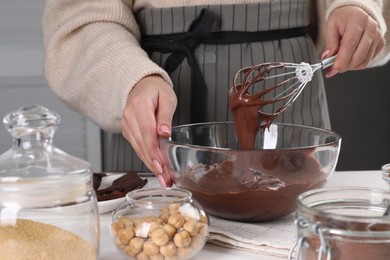 Woman mixing delicious chocolate cream with whisk at table indoors, closeup