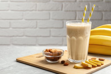 Photo of Banana smoothie in glass and nuts on light grey marble table against white brick wall. Space for text