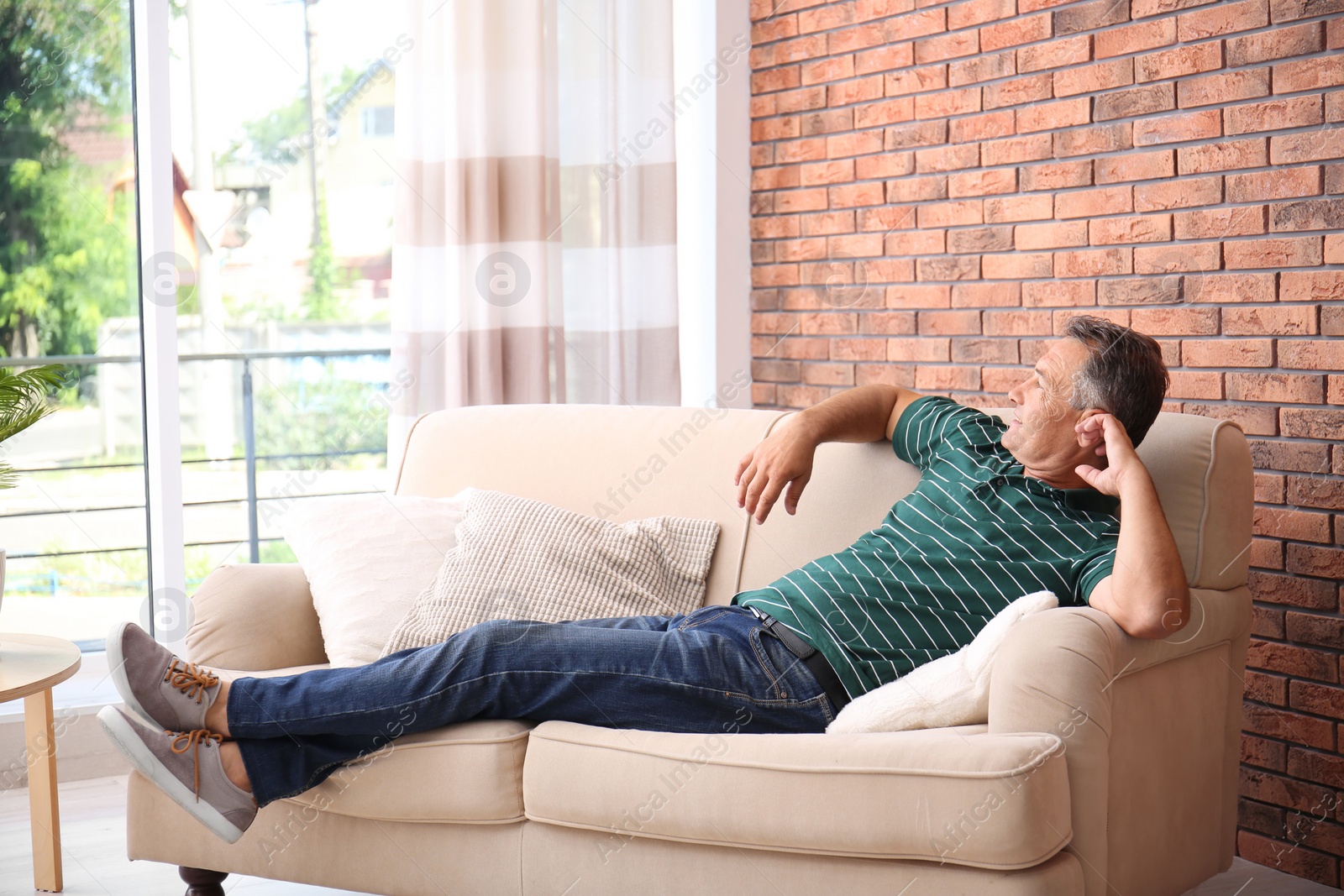 Photo of Man relaxing on sofa with comfortable pillows at home