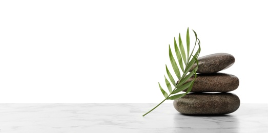 Photo of Stack of spa stones and tropical leaf on marble table against white background. Space for text