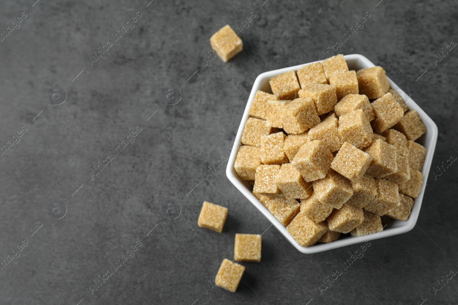 Photo of Brown sugar cubes in bowl on grey table, top view. Space for text