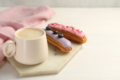 Photo of Cup of coffee and delicious eclairs covered with glaze on white wooden table. Space for text