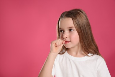 Photo of Cute little girl biting her nails on pink background, space for text