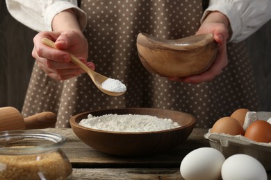 Making dough. Woman adding baking powder to flour at wooden table, closeup