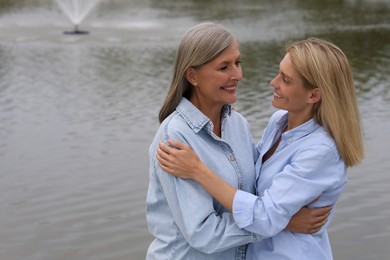 Happy mature mother and her daughter hugging near pond, space for text