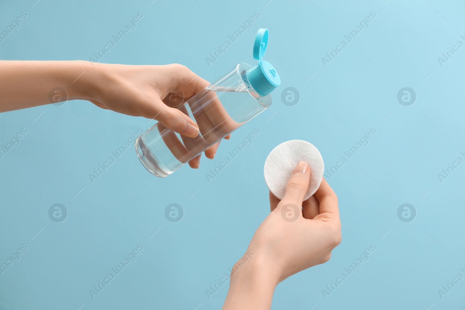 Photo of Woman pouring makeup remover onto cotton pad on light blue background, closeup