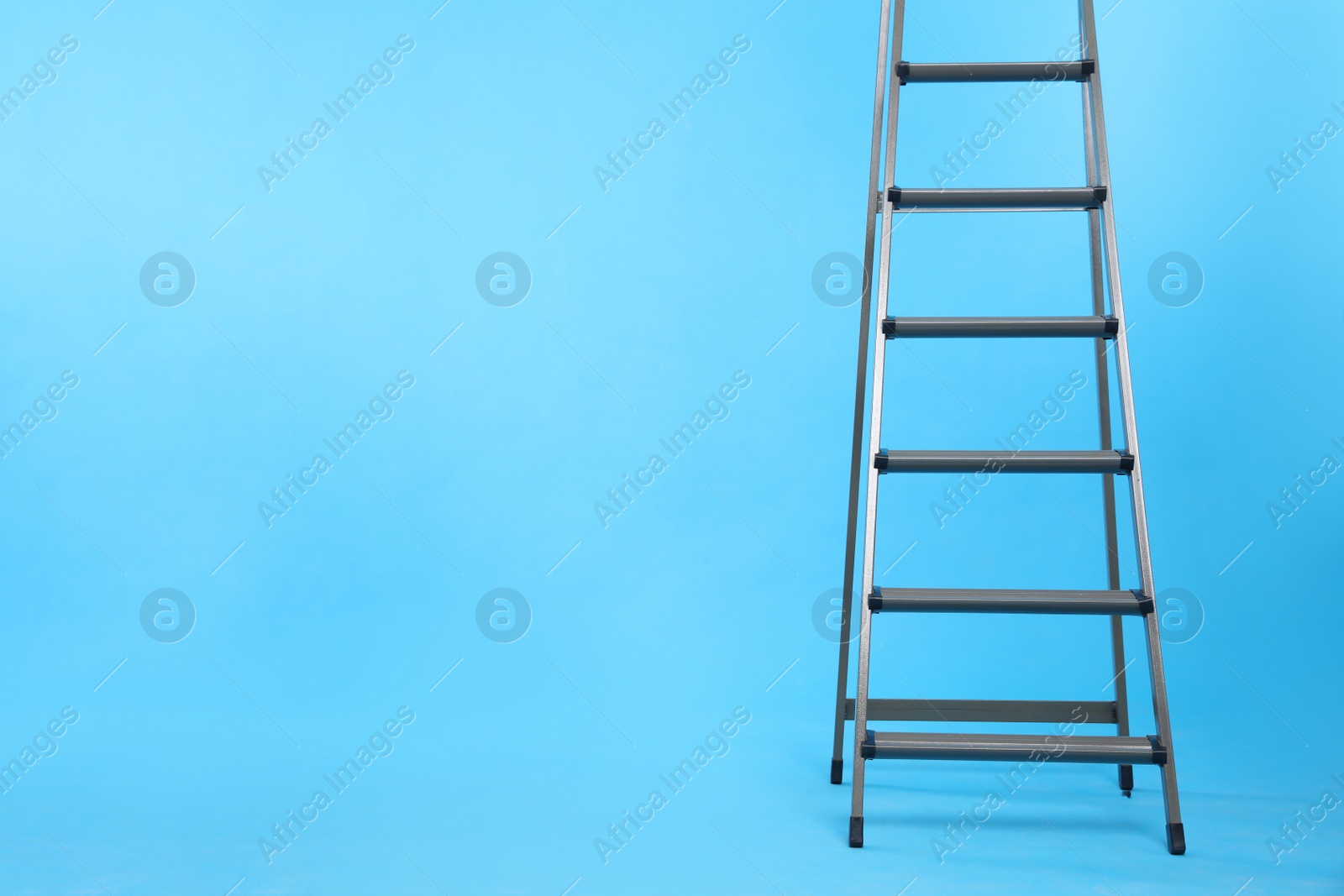 Photo of Metal stepladder on light blue background. Space for text