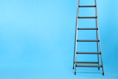 Photo of Metal stepladder on light blue background. Space for text