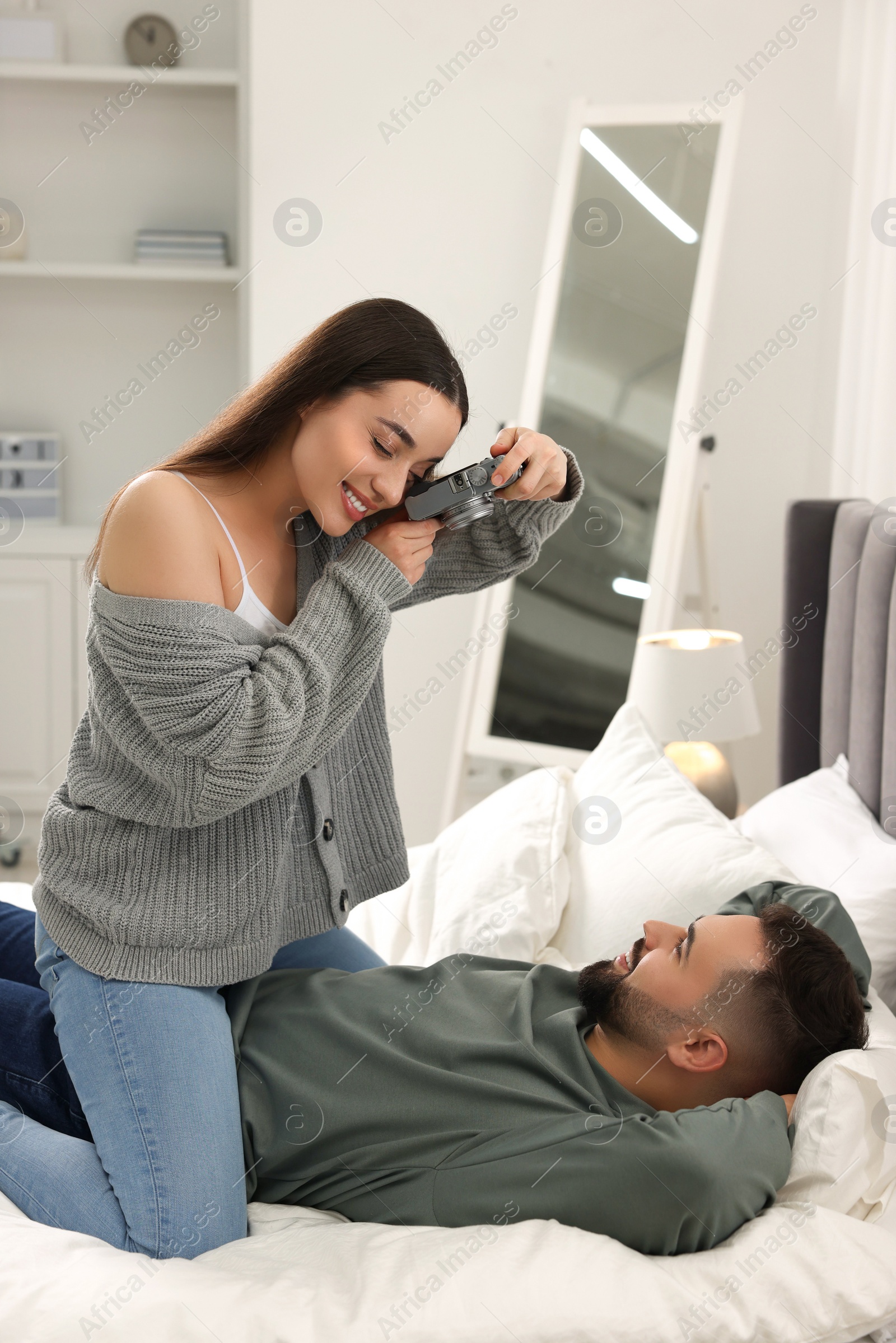 Photo of Happy young couple spending time in bedroom. Smiling woman taking photo of her boyfriend