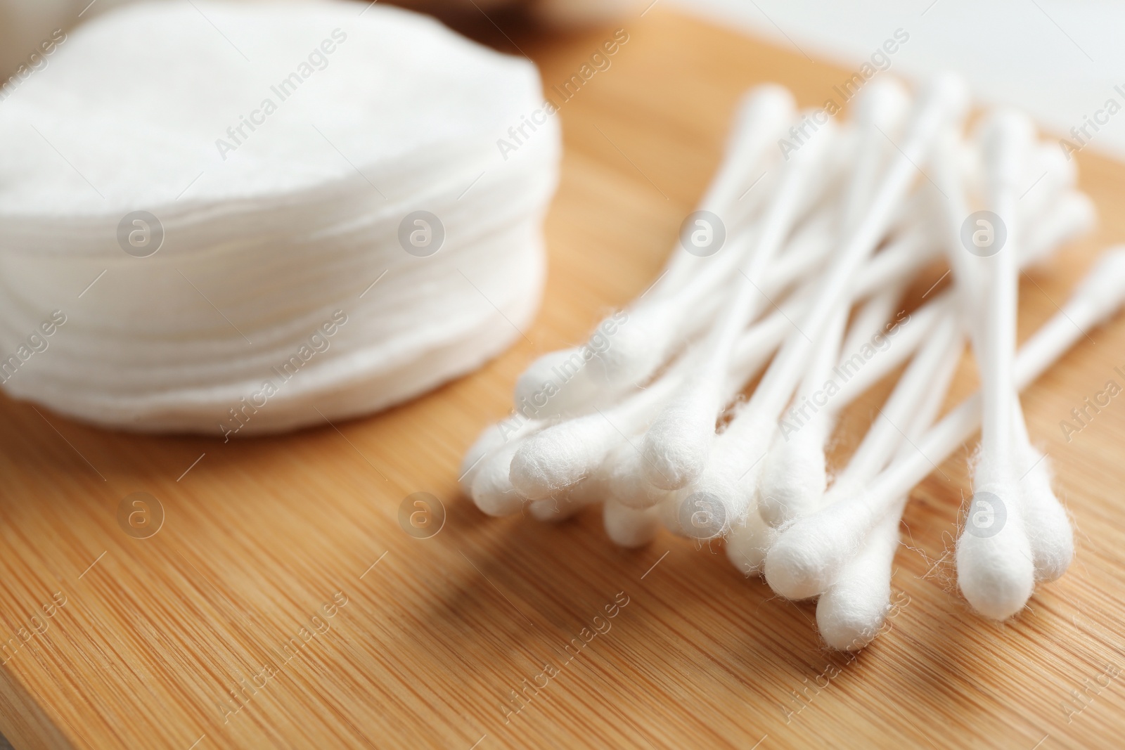 Photo of Cotton swabs and pads on wooden board, closeup