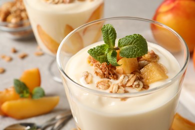 Photo of Tasty peach yogurt with granola, mint and pieces of fruit in glass on table, closeup