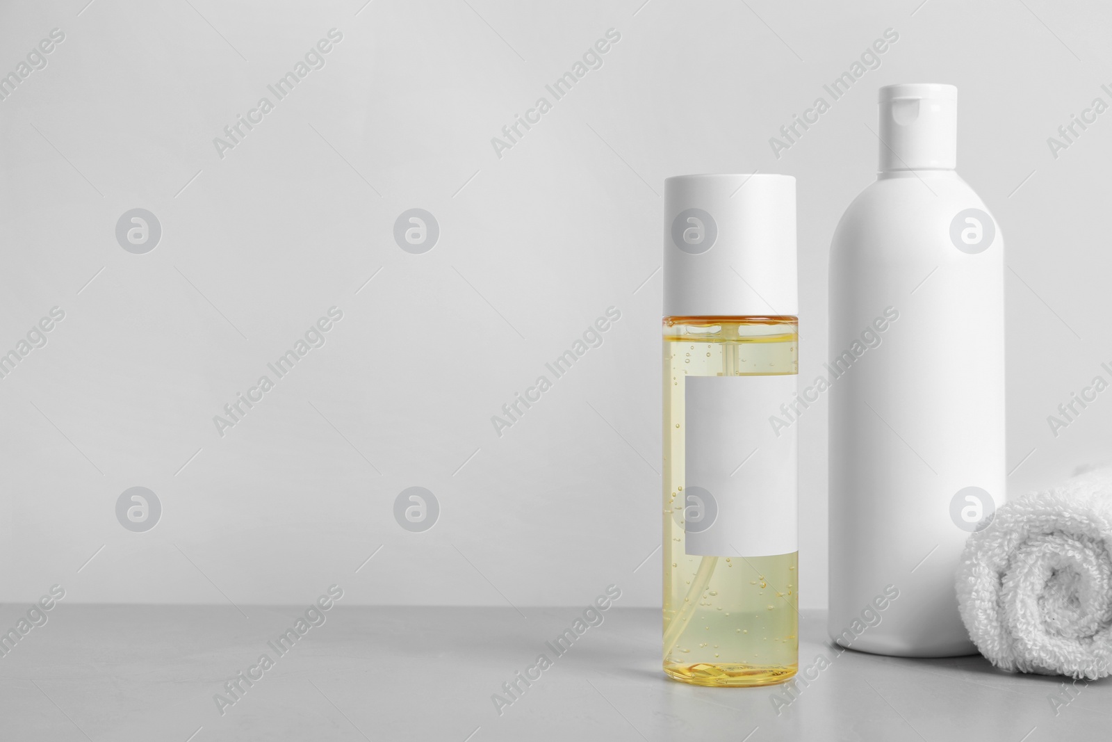 Photo of Bottles of cosmetic products and towel on grey table. Space for text