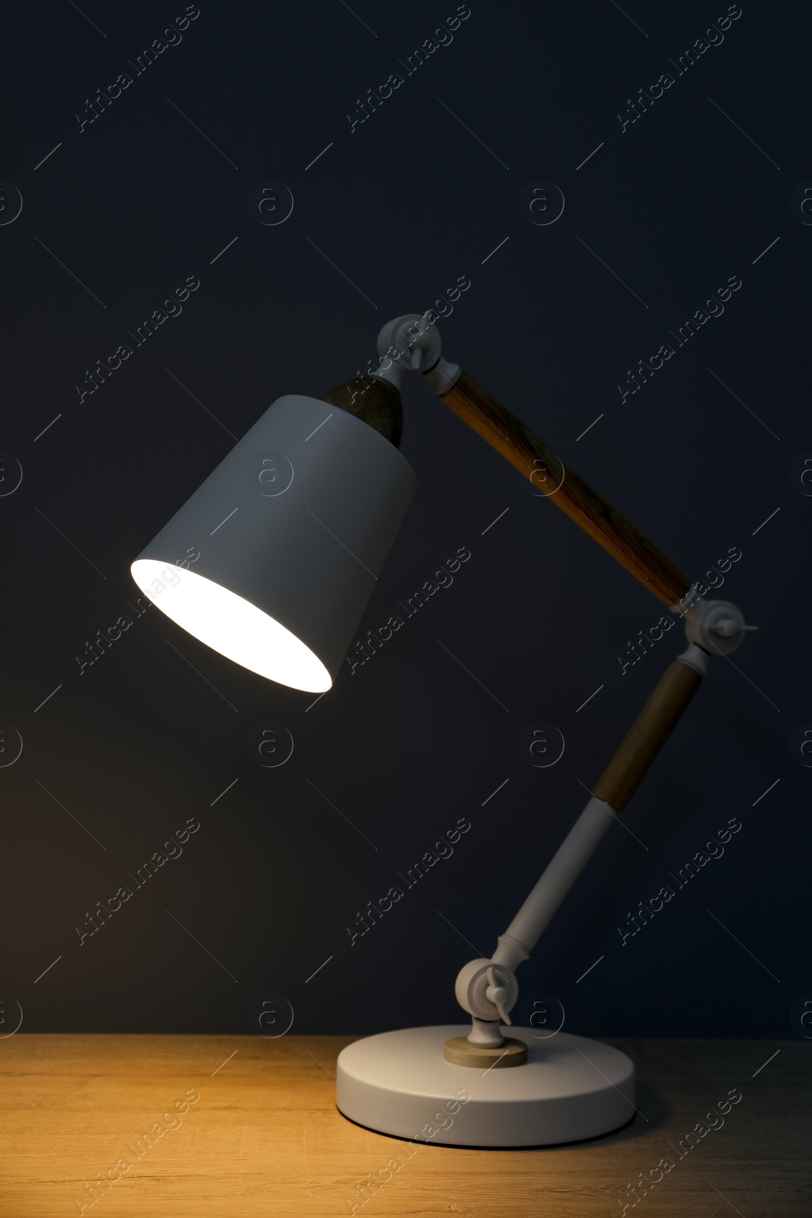 Photo of Stylish modern desk lamp on wooden table at night