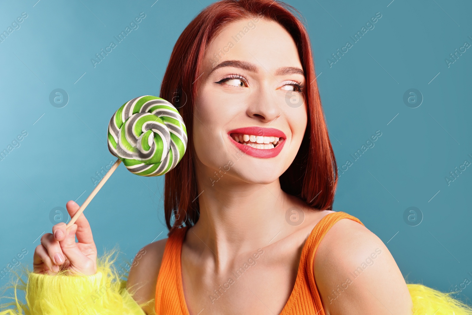 Photo of Happy woman with red dyed hair and green lollipop on light blue background