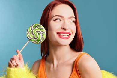 Happy woman with red dyed hair and green lollipop on light blue background