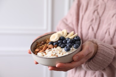 Photo of Woman holding bowl of tasty granola indoors, closeup. Space for text