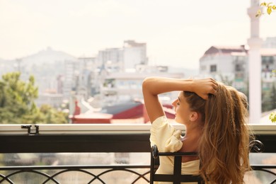 Photo of Beautiful young woman sitting on balcony, back view. Space for text