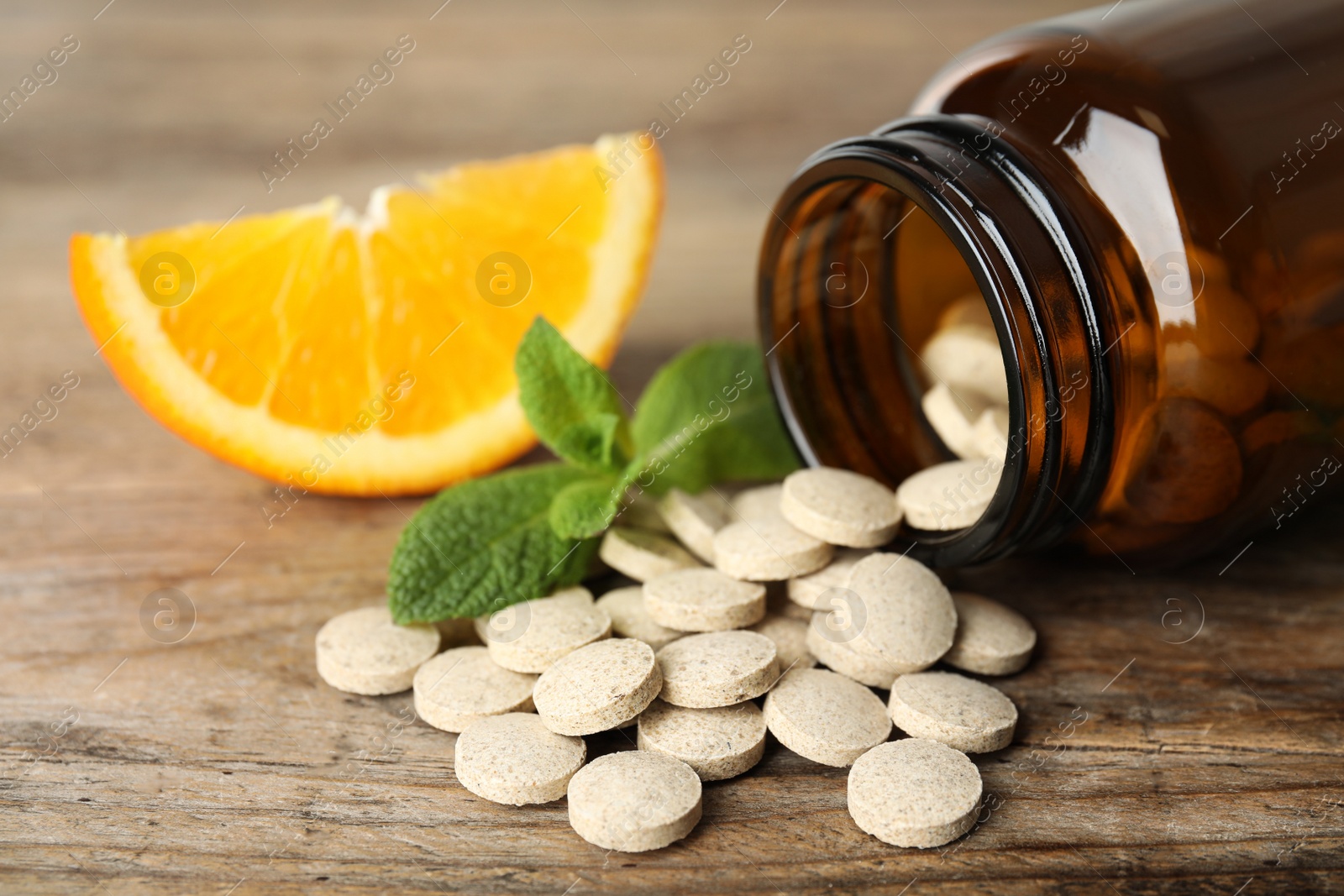 Photo of Bottle with vitamin pills, mint and orange on wooden table, closeup