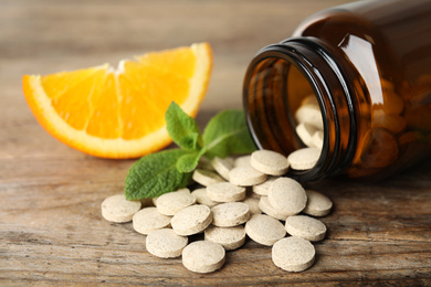 Photo of Bottle with vitamin pills, mint and orange on wooden table, closeup