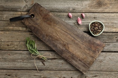 Photo of Cutting board, garlic, pepper and rosemary on wooden table, flat lay. Space for text