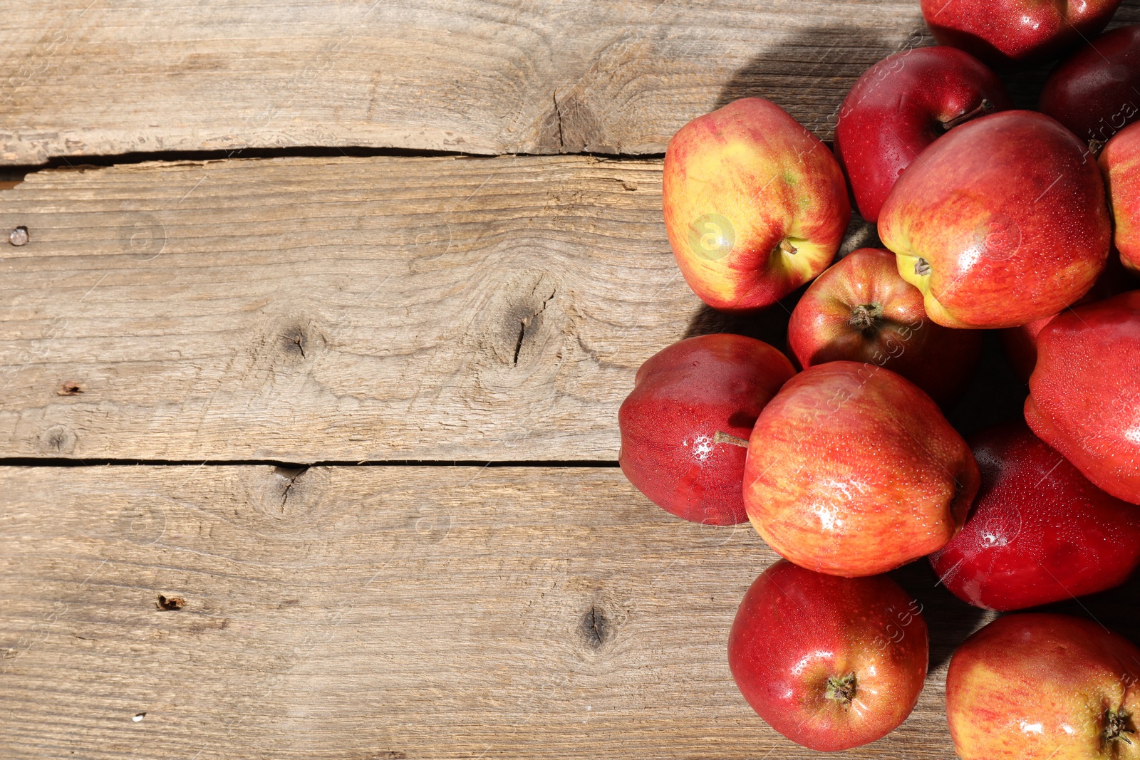 Photo of Many fresh apples with water drops on wooden table, top view. Space for text