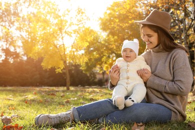Photo of Happy mother with her baby daughter sitting on grass in autumn park, space for text