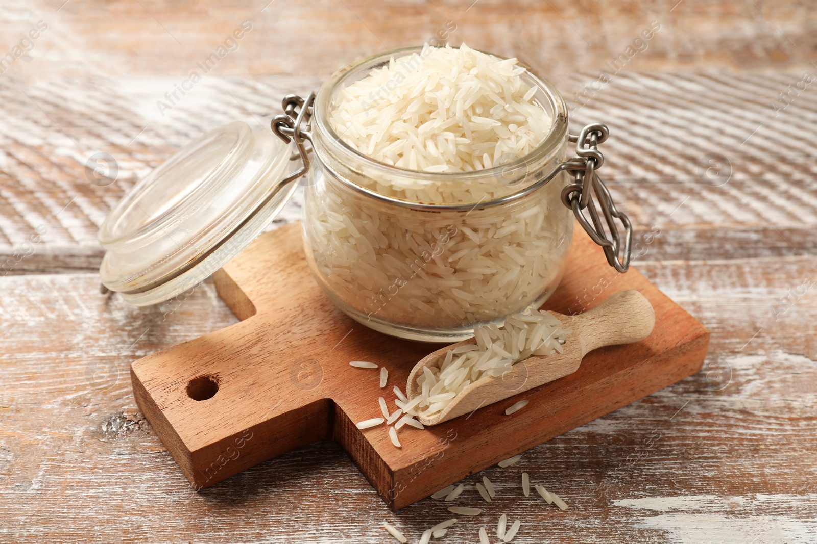 Photo of Raw basmati rice in glass jar and scoop on wooden table