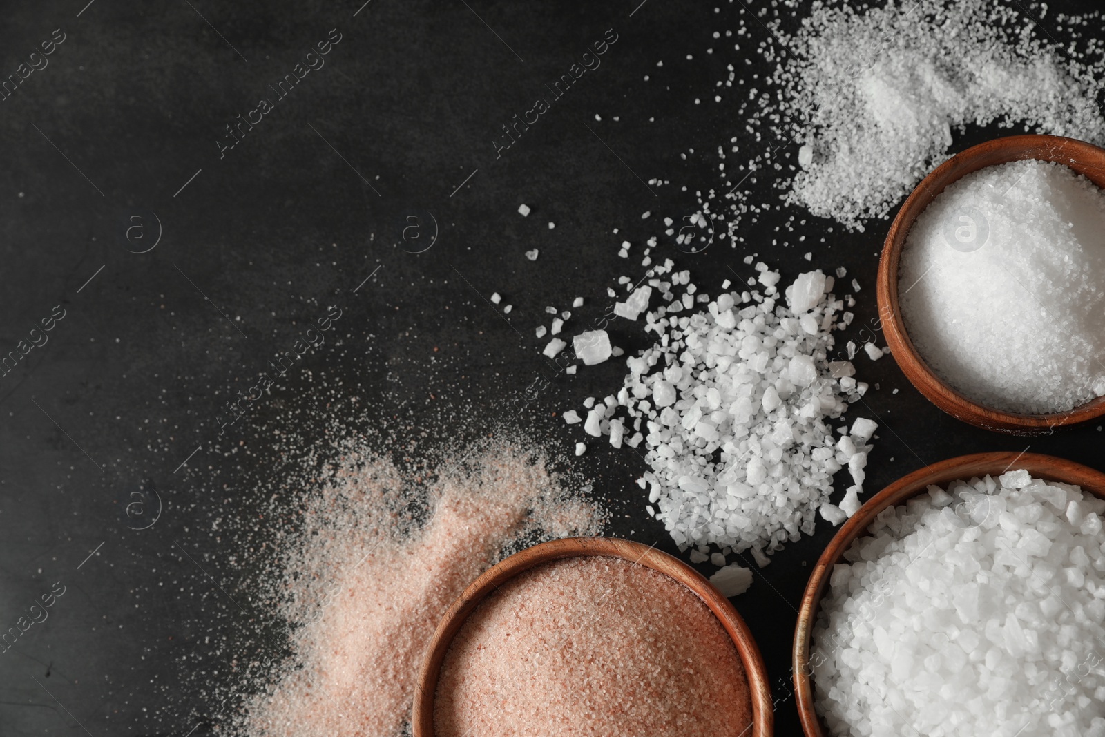 Photo of Different types of organic salt in bowls on black table, flat lay. Space for text