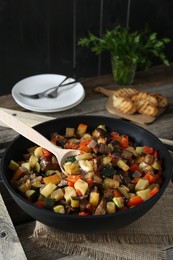 Photo of Delicious ratatouille and spoon in baking dish on wooden table