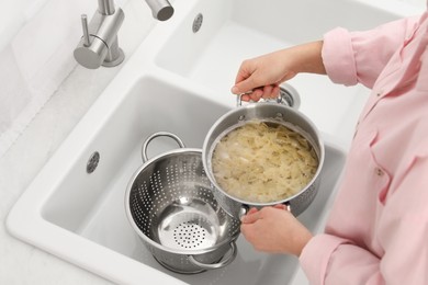 Woman draining pasta into colander at sink, above view